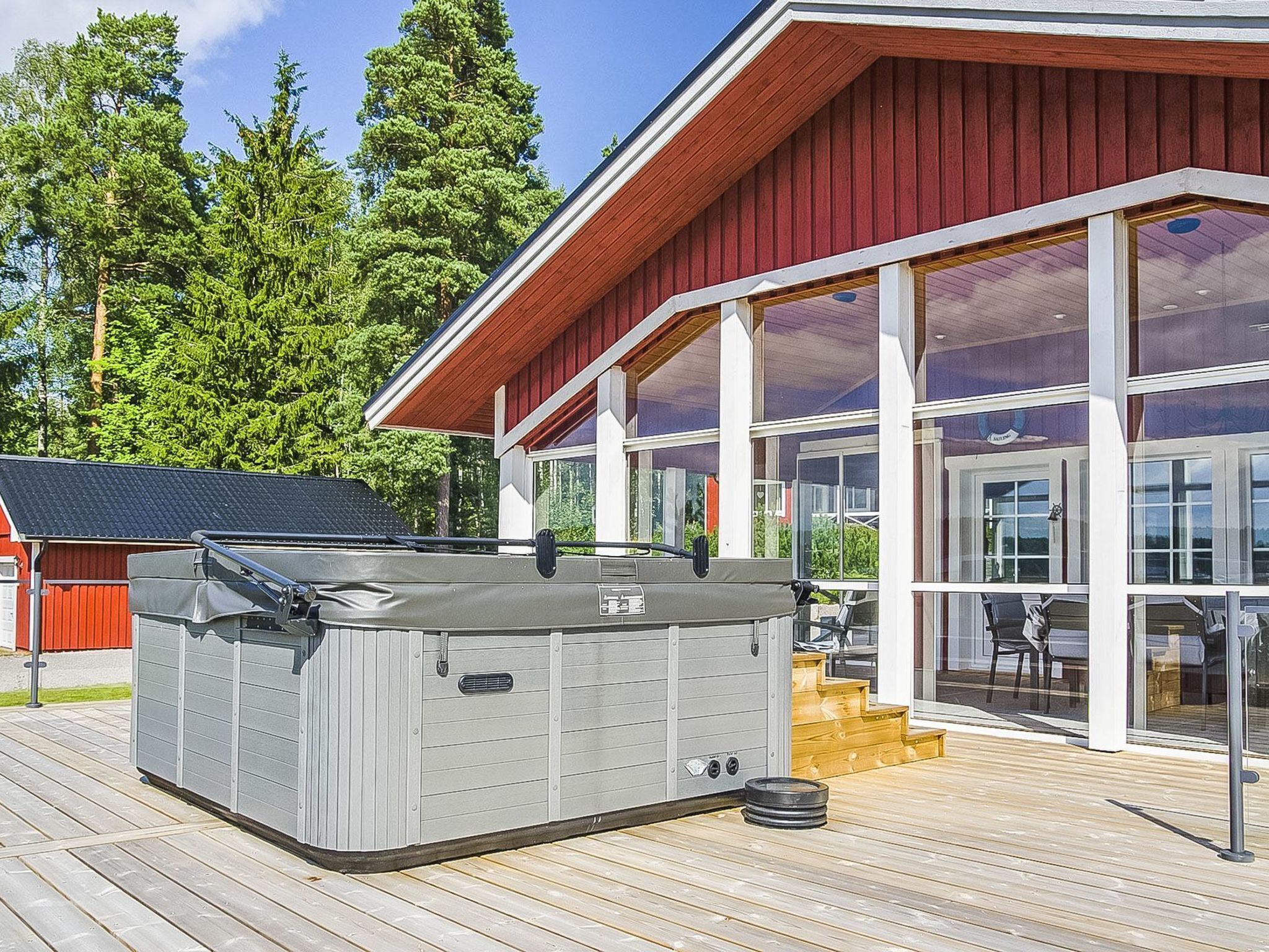 Un edificio moderno con amplios ventanales de vidrio, una terraza de madera y un jacuzzi.