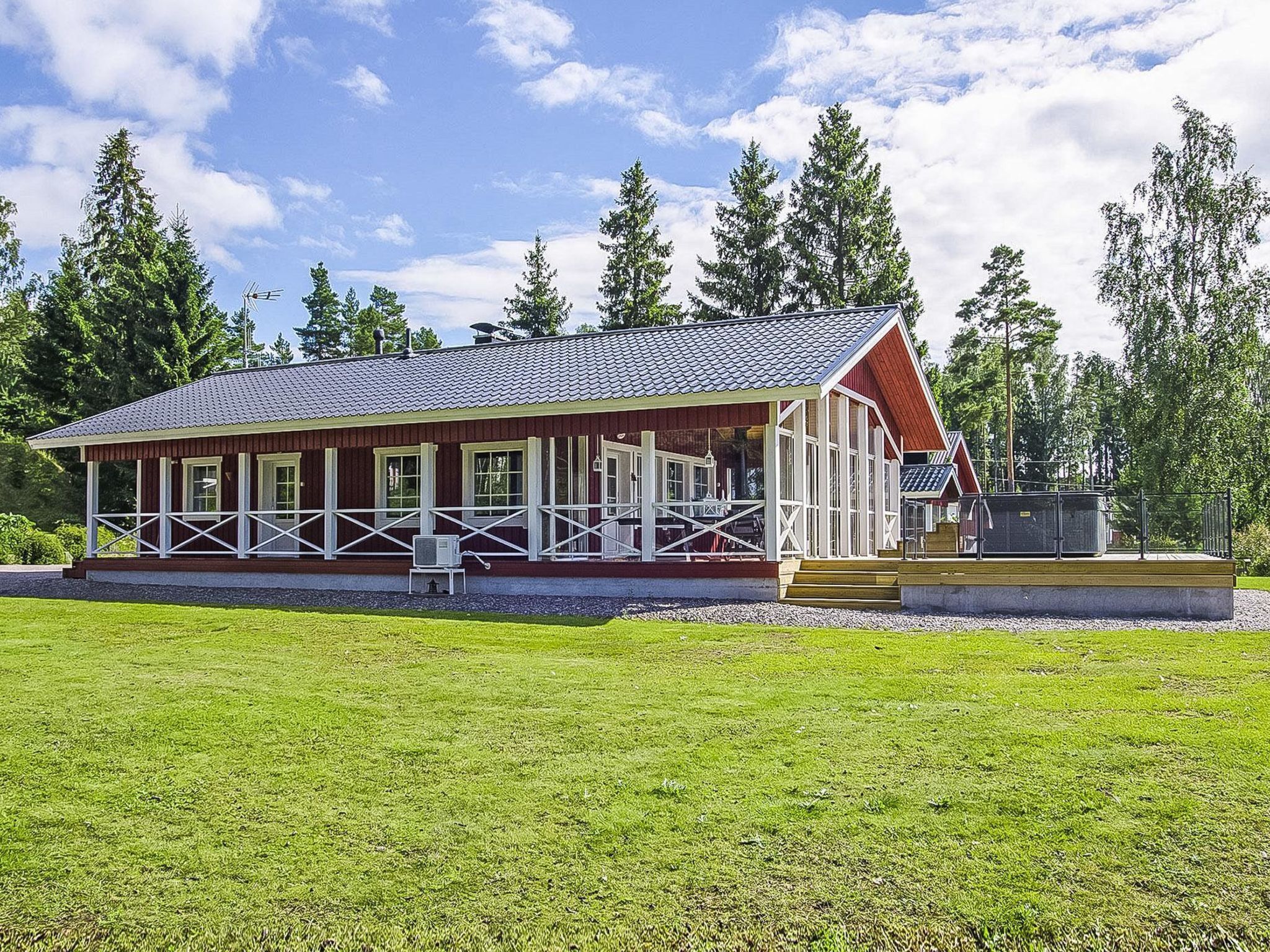 A wooden cabin with a porch, surrounded by a grassy field and tall trees.