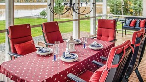 A dining area with a table set for four, red upholstered chairs, and a view of a lake through large windows. - Villa blomvik by Interhome (Porvoo)