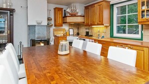 A modern kitchen with wooden cabinets, a large dining table, and a built-in stove. - Villa blomvik by Interhome (Porvoo)