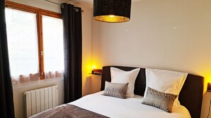 Un lit bien fait, avec une tête de lit sombre, une lampe de chevet et une fenêtre avec des rideaux.