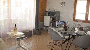 Un coin repas avec une table en verre, des chaises grises et une bibliothèque en arrière-plan.