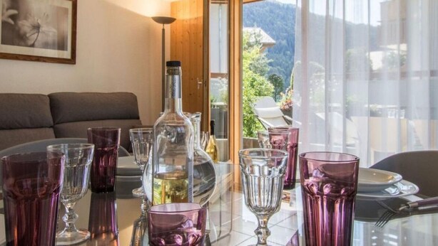 Un coin repas avec une table dressée pour quatre personnes, entourée de verres violets et d’une bouteille.