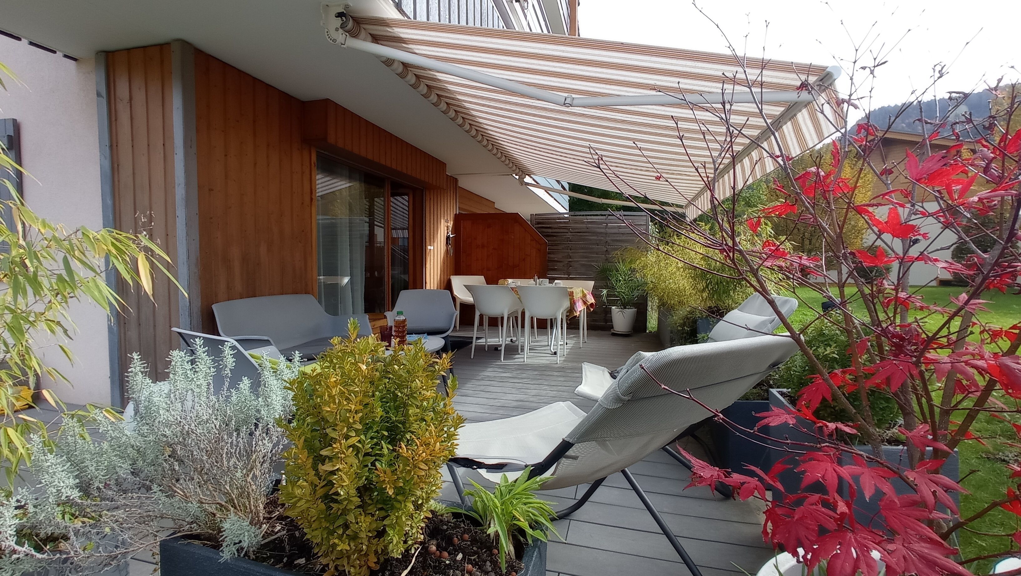 Une terrasse avec des sièges d’extérieur, un mur en bois et des plantes en pot.