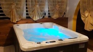 A hot tub in a room with wooden flooring and curtains.
