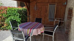An outdoor patio with a table and chairs, a wooden wall, and a hedge.