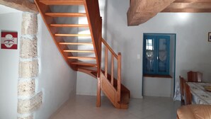 A wooden staircase in a room with a tiled floor, a blue door, and a dining area with chairs.