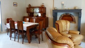 A dining area with a wooden table and chairs, a leather armchair, and a fireplace with a blue mantel.