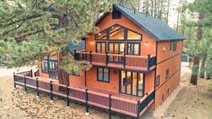 A two-story log cabin with a balcony, surrounded by pine trees.