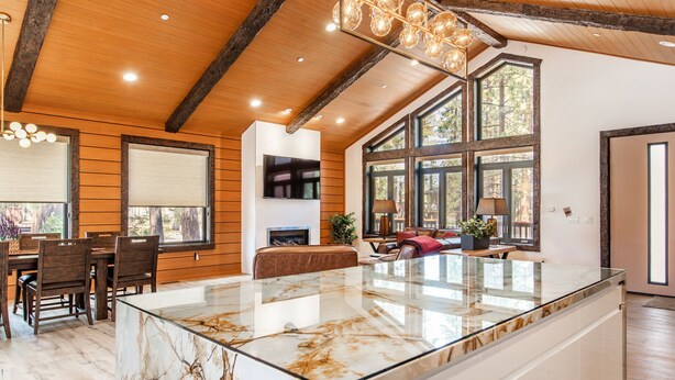 A spacious kitchen with a large marble island, wooden beams on the ceiling, and large windows providing natural light.