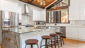 A modern kitchen with a large island, bar stools, and a view of the outdoors.