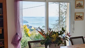 A room with a large window overlooking a coastal view, a dining table with chairs, and a potted plant in the center. - House with panoramic sea view and dream beach at 500 m (Crozon)