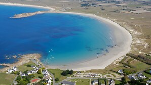An aerial view of a coastal area with a sandy beach, a small cluster of white houses, and a road leading to the beach. - House with panoramic sea view and dream beach at 500 m (Crozon)