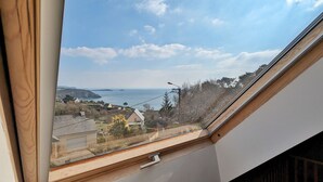 A view from a window with a wooden frame, overlooking a coastal landscape with houses, a road, and a clear sky. - House with panoramic sea view and dream beach at 500 m (Crozon)