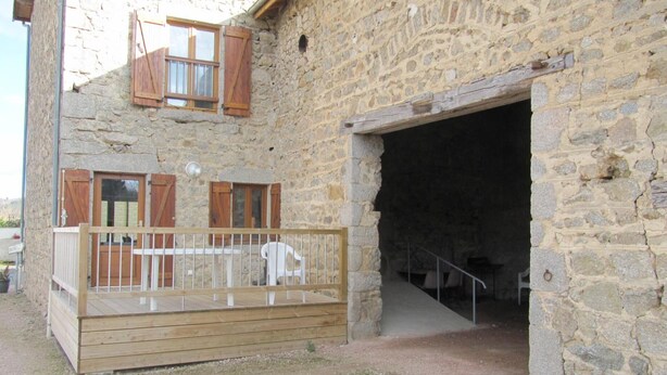Un bâtiment en pierre doté d’une terrasse en bois et d’un escalier menant à un intérieur sombre.