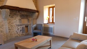 Un salon chaleureux avec une cheminée en pierre, une table basse en bois, un fauteuil gris et un canapé beige.