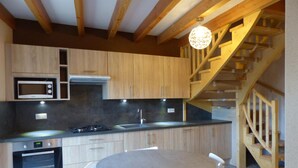 Une cuisine moderne avec des meubles en bois, un four à micro-ondes encastré, une cuisinière et une table de salle à manger ronde, accompagnée de chaises.