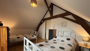 Ein gemütliches Schlafzimmer im Dachgeschoss mit zwei Betten, Holzbalken, einer Hängeleuchte und einem Schminktisch.