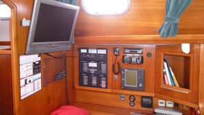 A control panel with various gauges and a screen, a small window with curtains, and a shelf with books. - Stays and unusual nights at the port of Morlaix on a 12-meter sailboat (Morlaix)