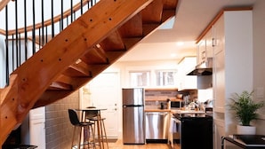 A modern kitchen with stainless steel appliances, a wooden staircase, and a cozy living area with a sofa and coffee table. - ★Ocean View Loft w/ Dedicated Hot Tub in Departure Bay. Treat Yourself Book Now★ (Nanaimo)