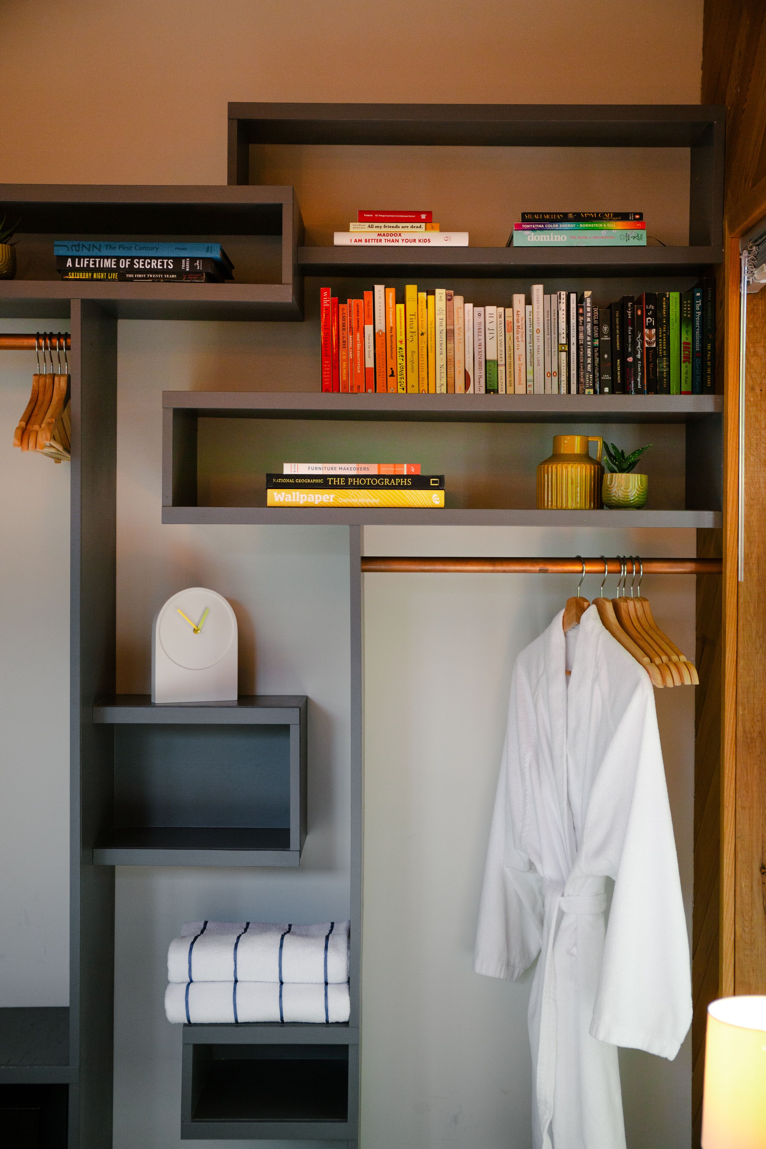 Una habitación de hotel con una estantería, un reloj, una bata y una toalla.
