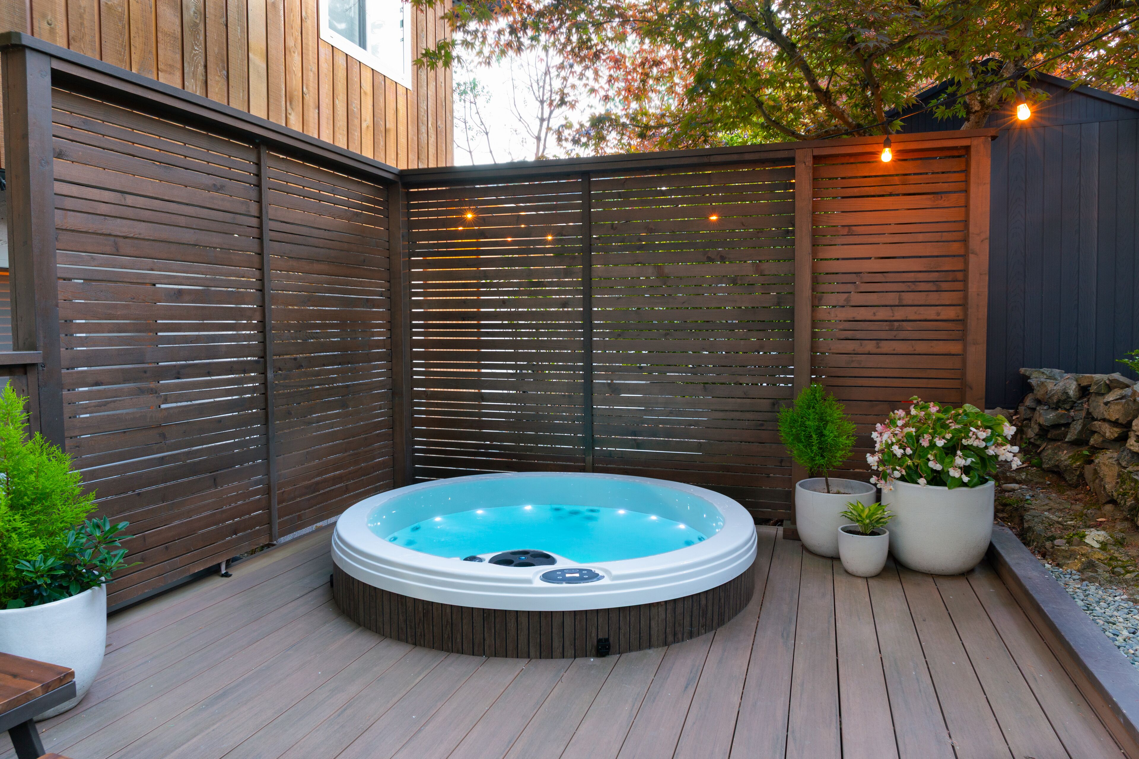 A hot tub in a wooden deck area with a wooden fence and potted plants.
