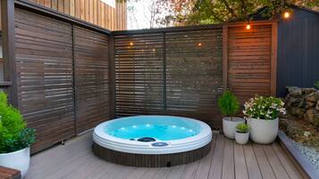 A hot tub in a wooden deck area with a wooden fence and potted plants.