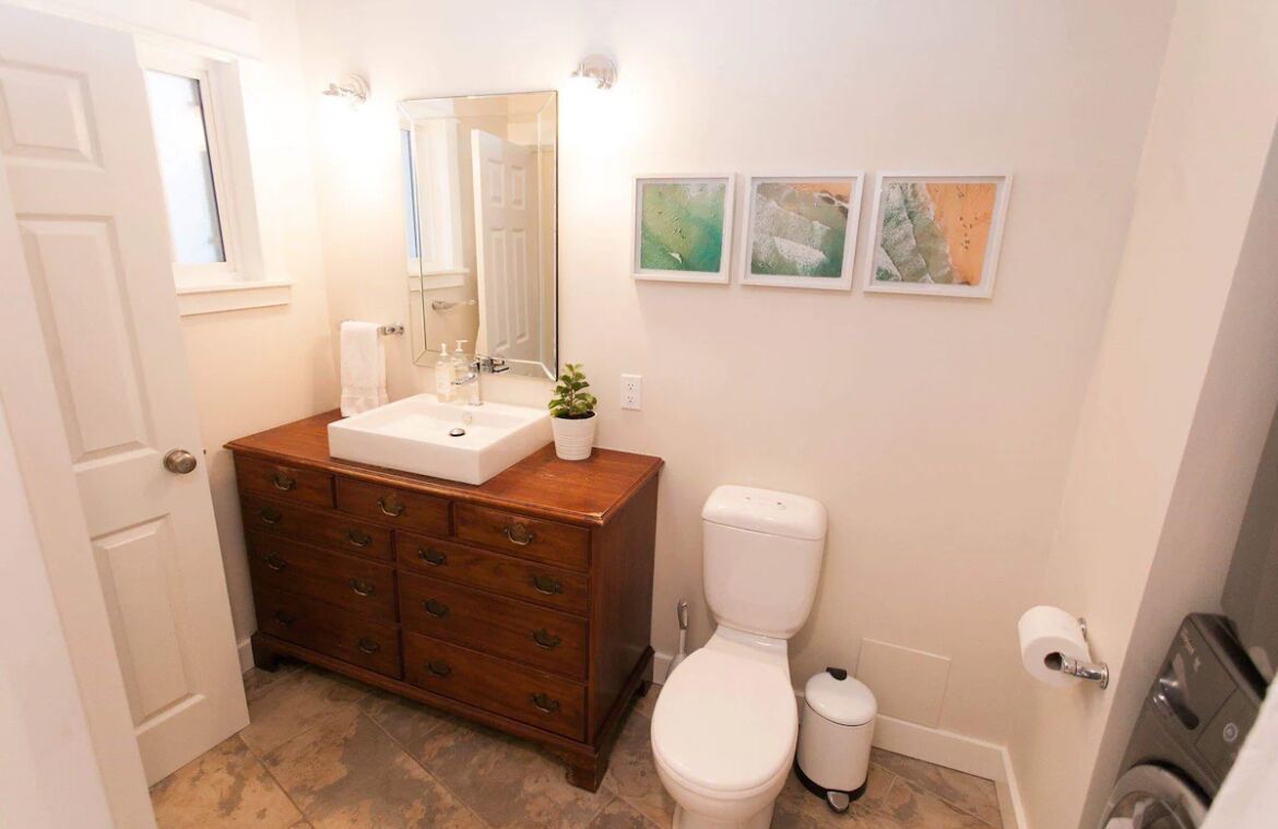 Een badkamer met een houten wastafel, een wit toilet en drie afbeeldingen in lijsten aan de muur.