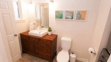 Een badkamer met een houten wastafel, een wit toilet en drie afbeeldingen in lijsten aan de muur.