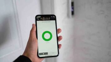 A hand holding a smartphone displaying a hotel room interface with a green loading circle.