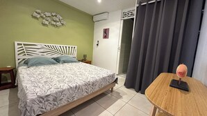 A bedroom with a bed, a nightstand, a wall-mounted air conditioner, a door, and a curtain. - ■ BEAUTIFUL T2 CLIMATISE IN VILLA SEA VIEW - RAVINALA MARTINIQUE ■ (LES TROIS ILETS)