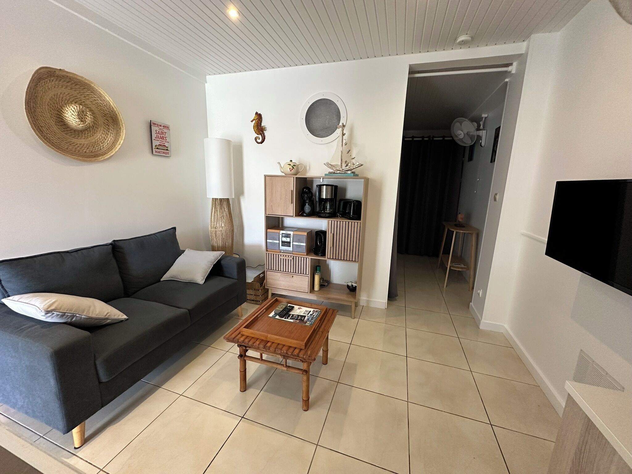 A modern living room with a black sofa, a wooden coffee table, a bookshelf, and a television mounted on the wall.