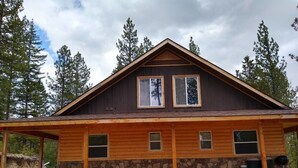 Eine zweistöckige Blockhütte mit Steinunterbau, großen Fenstern und einer Veranda.