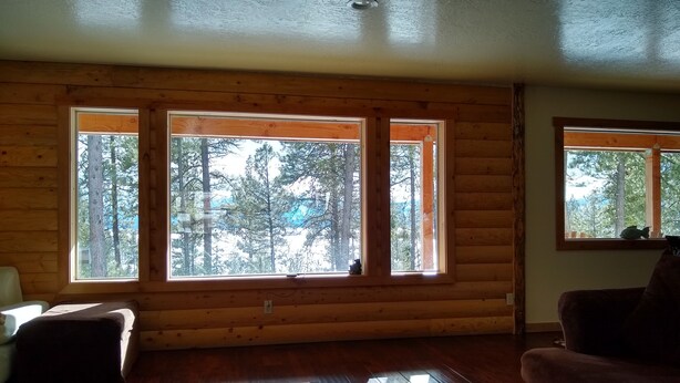 Ein rustikales Blockhaus-Interieur mit großen Fenstern, Holzböden und einem weißen, flauschigen Teppich.