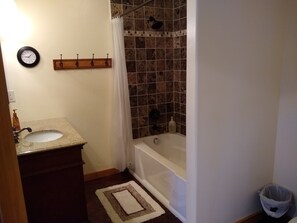 Un bagno con lavandino, specchio, orologio, doccia e cestino.