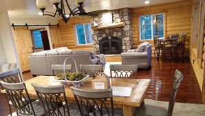 Ein gemütliches Blockhaus-Interieur mit Kamin aus Stein, einem Essbereich mit Granitarbeitsplatte und einem Wohnzimmer mit Sofa und Sesseln.