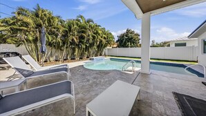 A covered outdoor area with a pool, lounge chairs, and palm trees. - Walk to beach or bask in your private pool, fun and newly renovated Beach House (Naples)