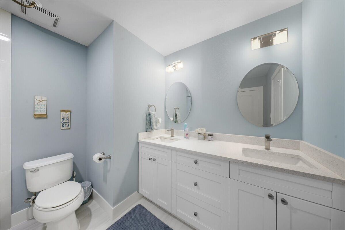 A bathroom with a white toilet, a sink with a mirror, and a vanity with drawers.
