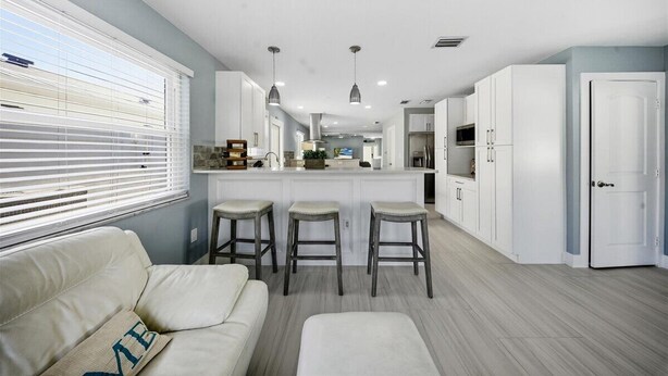 A modern kitchen with white cabinets, a central island with stools, and pendant lighting. - Walk to beach or bask in your private pool, fun and newly renovated Beach House (Naples)