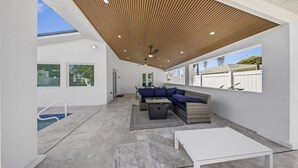 An outdoor living area with a pool, a wooden ceiling, and a seating arrangement. - Walk to beach or bask in your private pool, fun and newly renovated Beach House (Naples)