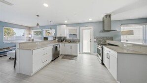 A modern kitchen with white cabinetry, a central island, and a built-in oven. - Walk to beach or bask in your private pool, fun and newly renovated Beach House (Naples)