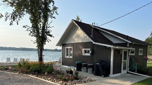 A small cabin with a dock, surrounded by a garden and a view of a lake. -  Escape to the Holiday House. Serenity of Sunsets, Lakeside boat dock included. (Lewiston)