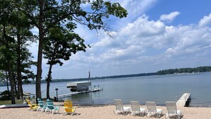 A beach with white lounge chairs and a covered boat docked near the water. -  Escape to the Holiday House. Serenity of Sunsets, Lakeside boat dock included. (Lewiston)