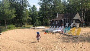 A sandy beach area with beach chairs and a small building in the background. -  Escape to the Holiday House. Serenity of Sunsets, Lakeside boat dock included. (Lewiston)