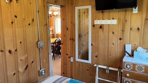 Een kamer met houten lambrisering, een bed, een dressoir, een televisie en een deur naar een andere kamer.