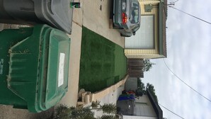 Une allée menant à une résidence, avec une voiture garée, une poubelle verte et une maison avec un garage.