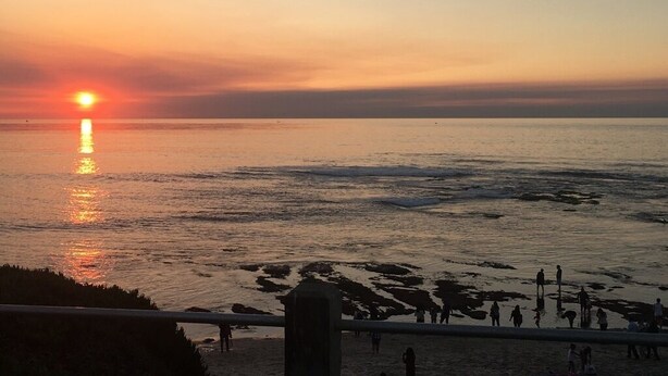 Un coucher de soleil sur une plage, avec des personnes se promenant le long du rivage.
