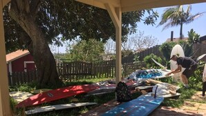 Un espace extérieur abrité, avec des planches de surf et une personne qui nettoie une planche de surf.