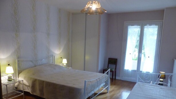 Une chambre à coucher avec un lit, des tables de chevet, une chaise, une table et une fenêtre avec des rideaux.