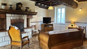 Ein gemütlicher Raum mit Kamin, Holzmöbeln, Fernseher und einem Fenster, das natürliches Licht hereinlässt.